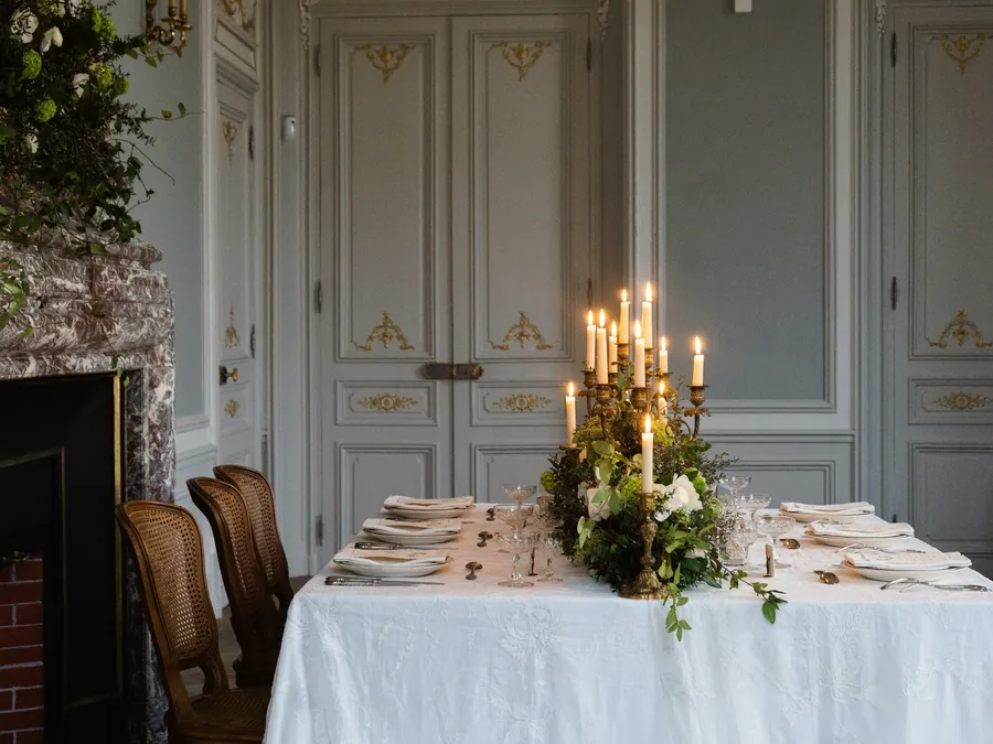 A candlelit dinner table set in an elegant country house dining room with a fireplace