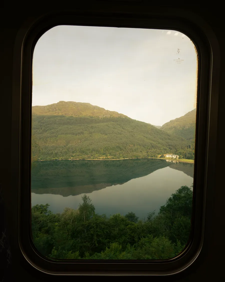 Green hills and a still lake seen through a train window